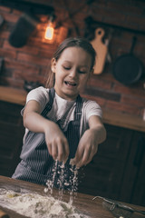 Poster - Young girl in apron pouring flour and preparing dough on kitchen table.