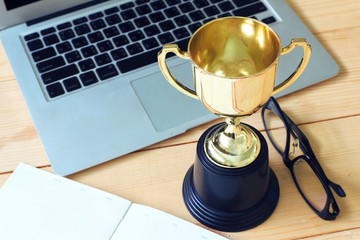 Wall Mural - trophy and laptop and glasses and note book on wood table, win concept.