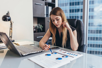 Female businesswoman readind financial report analyzing statistics pointing at pie chart working at her desk