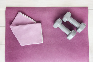 Open exercise mat, two dumbbells and sport towel on background with copyspace. Concept for home workout, fitness and gym.