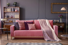 Front View Of A Pink Sofa With Pillows And Blanket, Vintage Cupboard In The Background In A Glamorous  Living Room Interior
