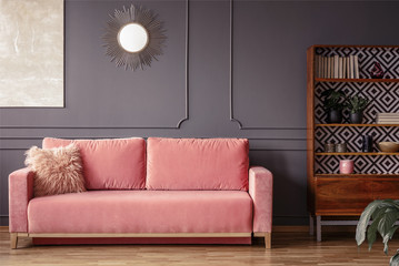 Wall Mural - Simple, pink sofa with a fur pillow next to a wooden cupboard in living room interior with grey wall and mirror