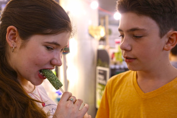 Wall Mural - vegan dessert candy with spirulina on stick with two teenager kids boy and girl close up photo