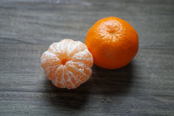 peeled and unpeeled clementines or tangerines or mandarin oranges on rustic wooden background with selective focus