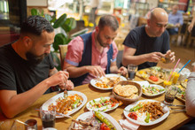 Group Of Muslim People In Restaurant Enjoying Middle Eastern Food. Selective Focus