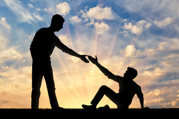 Silhouette of a man giving a helping hand to another man who fell to the ground