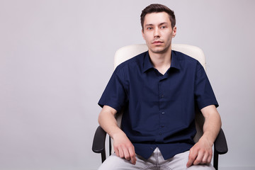 Portrait of young businessman in casual shirt sitting on a chair over grey background in studio photo