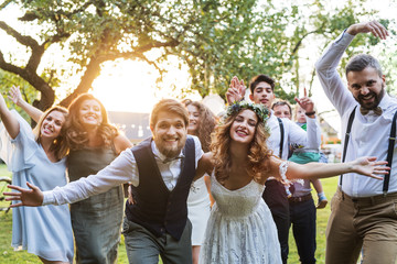 Bride, groom, guests posing for the photo at wedding reception outside in the backyard.