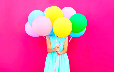 Cool girl is hides her head an air colorful balloons having fun over pink background