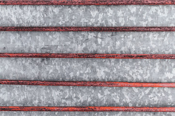 Metal background of an old rusty vertical grille and galvanized metal sheet. There are remains of paint.