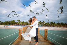 Seagulls Fly Over Gorgeous Wedding Couple Kissing On The Wooden Quay Over The Sea