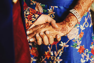 Canvas Print - Hindu groom holds bride's hand covered with henna tattoos