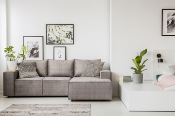 Patterned pillow on grey corner sofa in living room interior with plant and poster. Real photo