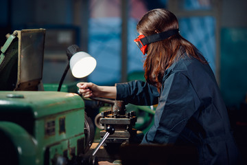 Young woman is practicing on shop floor lathe for college. Concept female profession carver for iron.