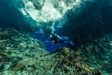  woman diver underwater at the entrance of a cave with sunrays