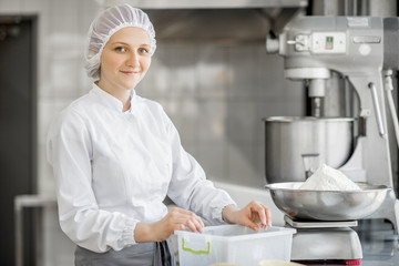 Portrait of a woman confectioner in uniform weighing ingredients for pastry at the bakery manufacturing