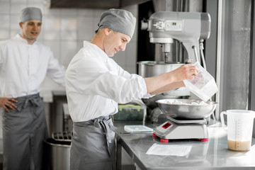 Two handsome male confectioners in uniform weighing ingredients for baking at the manufacturing