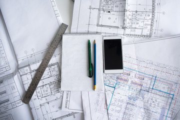 Green pen, blue pencil, white cellphone, metal ruler, notepad and some paper draws of a house (home) are laying down on white table. All staff is for a architecture negotiation.