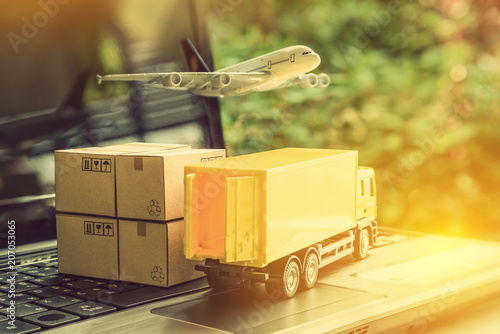 Fotomural Air courier / freight forwarder or shipping service concept : Boxes, a truck, white plane flies over a laptop, depicts customers order things from retailer sites via the internet and ship worldwide