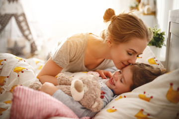 mother wakes her daughter in bed in morning