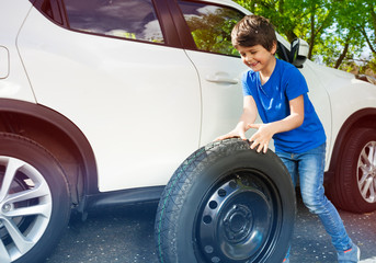 Happy little boy rolling donut tire next to a car