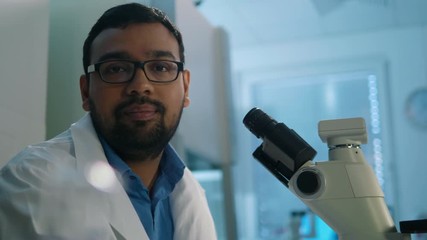 Wall Mural - young male life scientist doing research in laboratory looks directly at the camera and smiles.