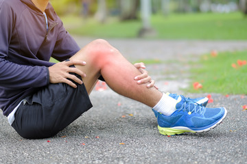 Young fitness man holding his sports leg injury, muscle painful during training. Asian runner having calf ache and problem after running and exercise outside in summer