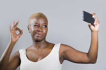 young beautiful and happy black afro American woman smiling excited taking selfie picture portrait giving ok hand sign blinking eye