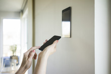Woman's Hands Adjusting Digital Tablet Mounted On Wall With Smartphone