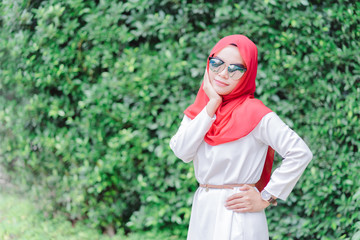 Wall Mural - Portrait of happy young muslim woman red hijab wear fashion glasses over blurred the green field background.