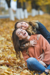 Young pretty girls having fun outdoors in autumn background. Cheerful friends in the fall time