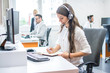 © Bojan - Side view of beautiful young lady working in office. Customer support worker taking notes while talking with client via headset at office desk.