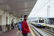 Portrait Of Young Man Waiting For Train On Railway Platform