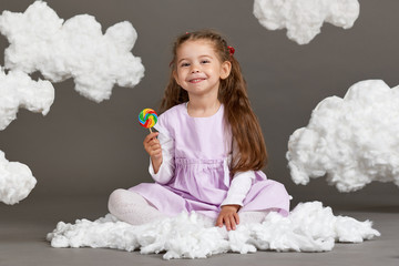 girl girl eating candy and playing with clouds, shooting in the studio on a gray background, happy childhood concept