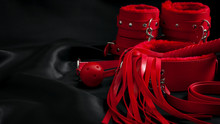 Bondage, Kinky Adult Sex Games, Kink And BDSM Lifestyle Concept With A Pair Of Red Leather Handcuffs, Flogger, Ball Gag And A Coller With A Leash Attached On Black Silk With Copy Space