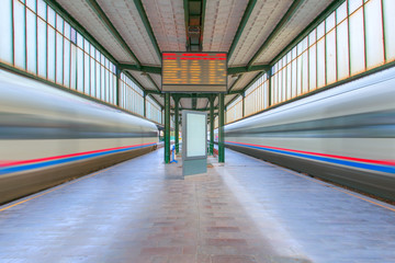 Sticker - Two white high speed train runs on rail tracks with Blurred Train schedule board and watch on platform . Train in motion