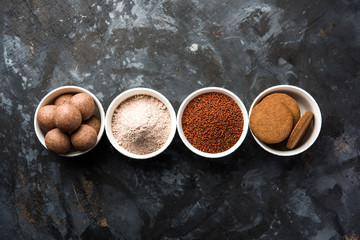 Nachni / Ragi laddu and biscuits or cookies made using  finger millet, sugar and ghee. It's a healthy food from India. Served in a bowl or plate with raw whole and powder. Selective focus