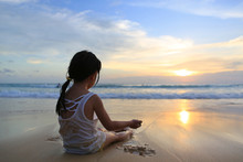 Asian Girl Sitting And Playing Sand On The Beach At The Sunset.