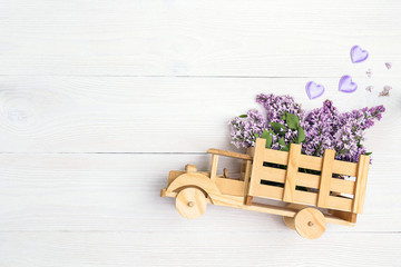 Poster - Wooden toy truck with lilac flowers in the back on white wooden background. Space for text.