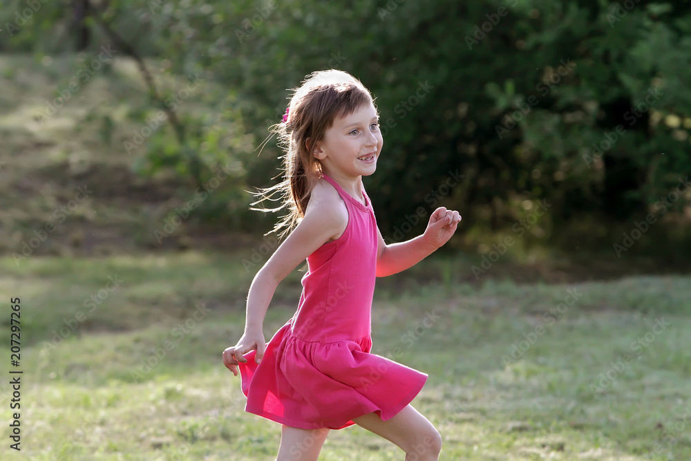 A beautiful little girl in a pink dress emotionally happily runs ...