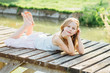 © Iryna - Portrait of cute blond 7 years old girl lying on the wooden bridge at the summer time.