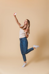 Canvas Print - Full length photo of positive blond woman 20s wearing casual clothing taking selfie photo on cell phone, isolated over beige background