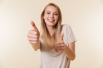 Poster - Image of attractive caucasian woman wearing casual clothing smiling and showing thumb up meaning good result or choice, isolated over beige background in studio