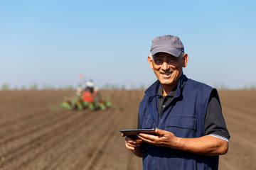 Senior farmer in field examining sowing and holding tablet in his hands.