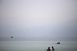 several people bathe in the Dead Sea against the cloudless sky and the Judean mountains in the gray haze in the distance