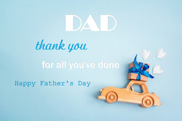 Wall Mural - Father's Day greeting message with wooden toy car with a gift box on the roof on blue background