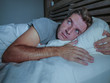© TheVisualsYouNeed - restless worried young attractive man awake at night lying on bed sleepless with eyes wide opened suffering insomnia sleeping disorder depressed