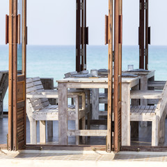 Wall Mural - Table and wooden chairs in empty cafe next to the sea water on the beach, Thailand