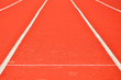 Czerwona tartanowa bieżnia i białe pasy rozdzielające tory dla biegaczy.