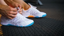 Fit Woman Seated On The Floor Of A Gym Tying Shoelaces Sneakers. Healthy Lifestyle. Sport And Cardio Workout Concept